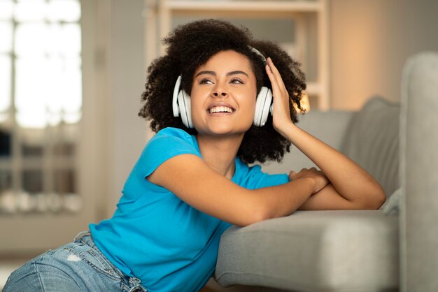 Thoughtful glad young curly african american lady in wireless headphones listen music enjoy spare time