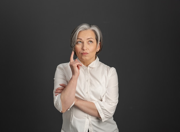 Thoughtful graying woman with forefinger pointing up on black wall