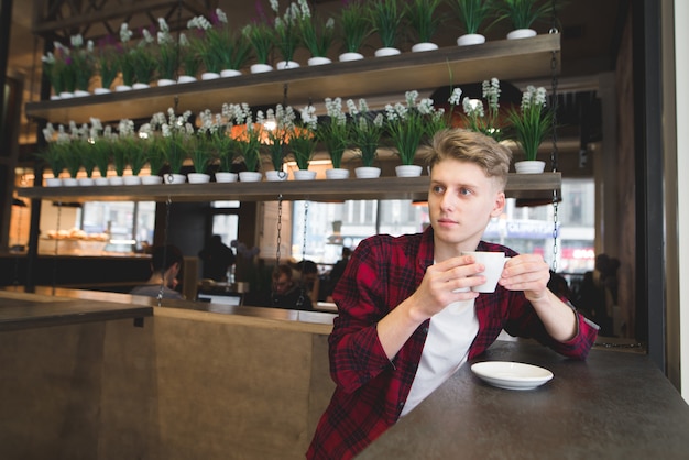 Вдумчивый, красивый молодой человек сидит в кафе, пьет кофе и смотрит в сторону.
