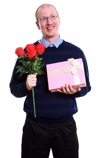 Thoughtful happy man smiling while holding red roses and gift box