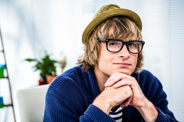 Thoughtful hipster businessman looking at the camera in his office