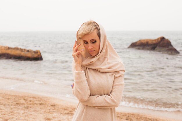 Thoughtful hipster woman wearing dress near sea in autumn