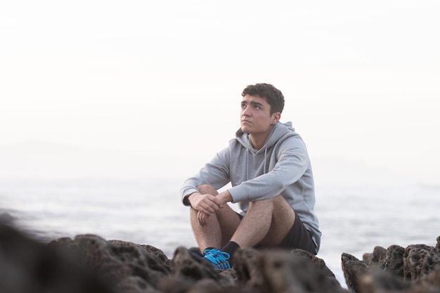 岩の上に屋外で座っている思いやりのあるヒスパニック系のティーンエイジャー。青年期の概念におけるうつ病と不安