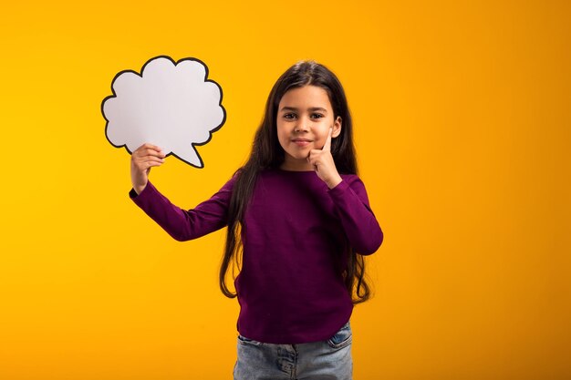 Photo thoughtful kid girl holding cloud bubble card over yellow background dreaming concept