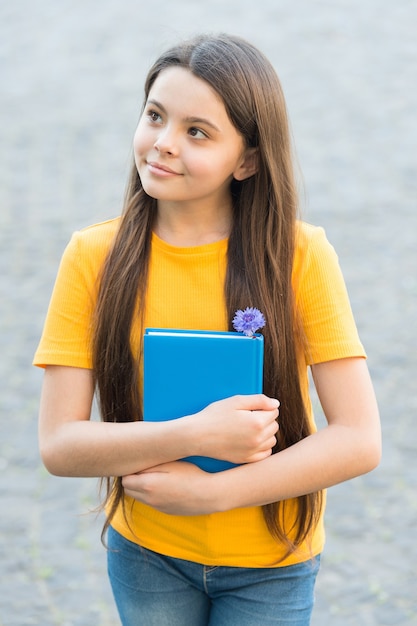 Thoughtful kid holding book. small girl thinking outdoor. school education in modern life. back to school. teen girl love reading. notebook for writing memories. child with school journal.