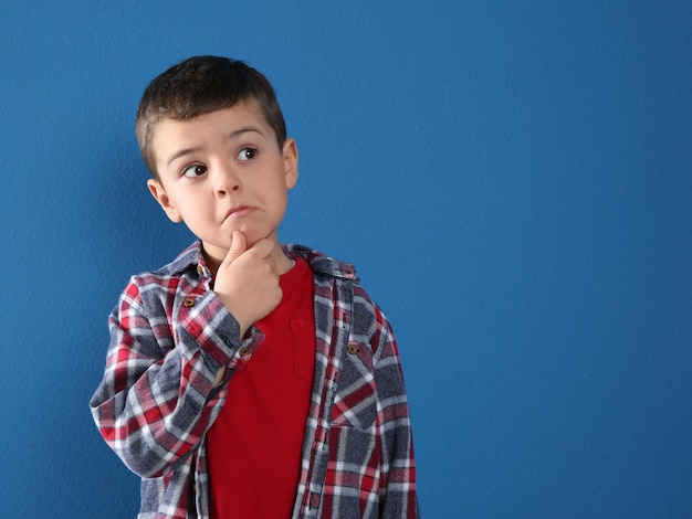 Thoughtful little boy in casual outfit on blue background