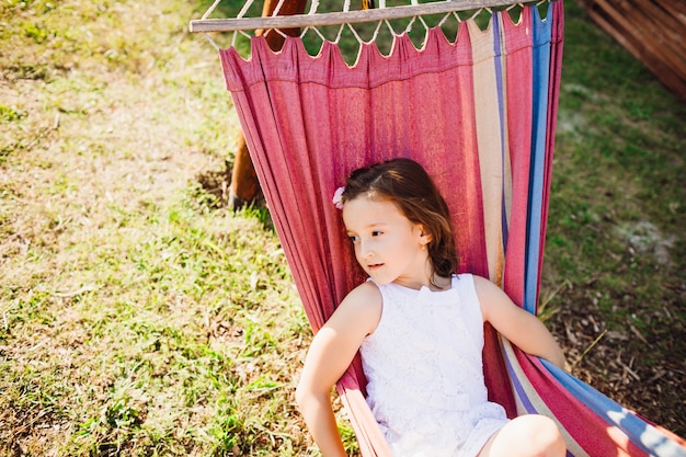 Thoughtful little child lies on pink hammock in the shadow