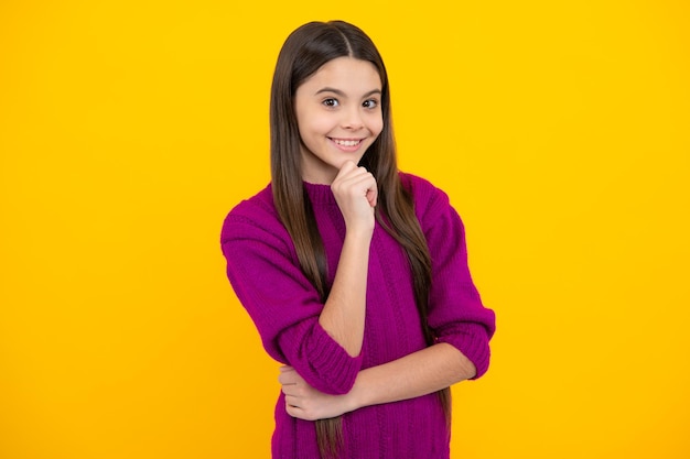 Thoughtful little teenager girl touch chin with finger thinking pensive lovely child making imagining idea posing isolated on yellow studio background