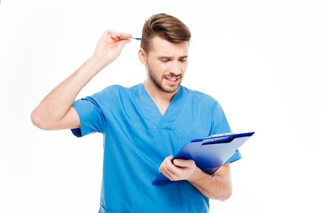 Thoughtful male doctor standing with clipboard isolated on a white background