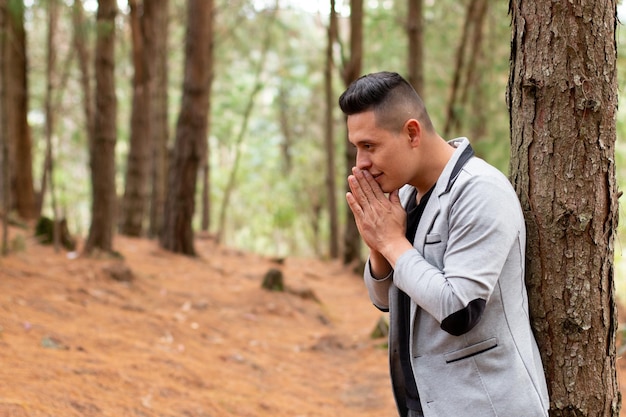 Thoughtful man clasping his hands together near his mouth. Man praying in the forest.