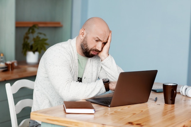 L'uomo premuroso sta scrivendo su un computer portatile, lavora a casa, lavora online, coronavirus