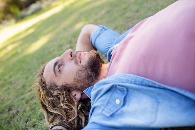 Photo thoughtful man lying on grass with hand behind head