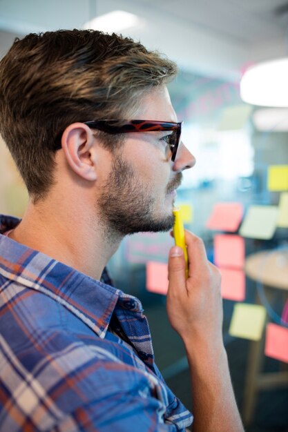 Photo thoughtful man reading sticky notes on the glass wall in office