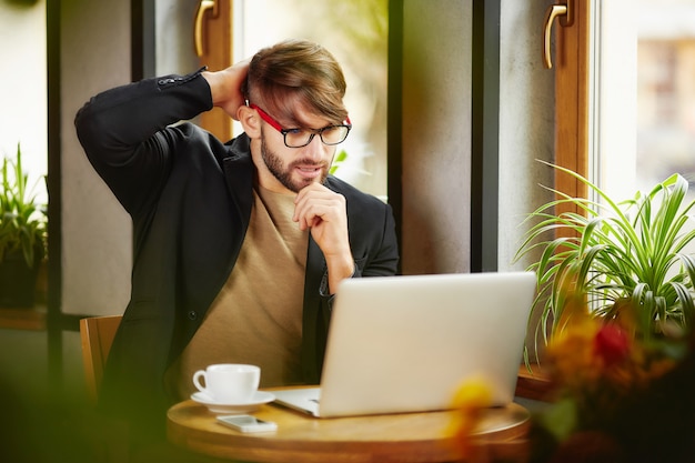 Thoughtful man scratching head at laptop