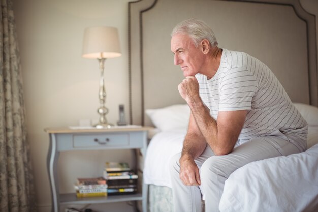 Thoughtful man sitting on bed in bedroom