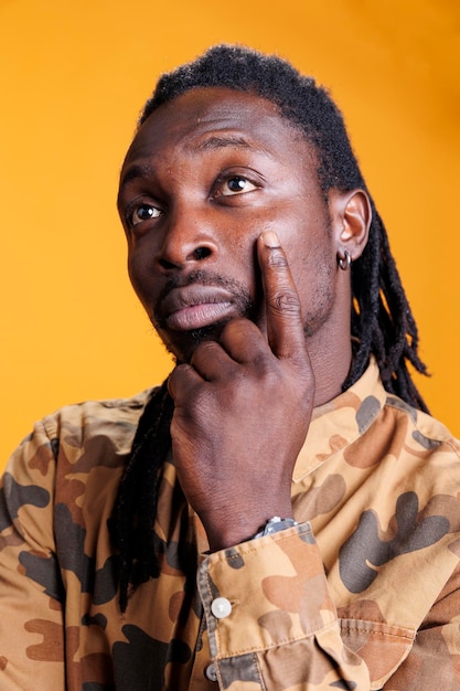 Thoughtful man thinking at business ideas in studio over yellow background, feeling confused and wondering about idea and question. Pensive african american person showing contemplative expression