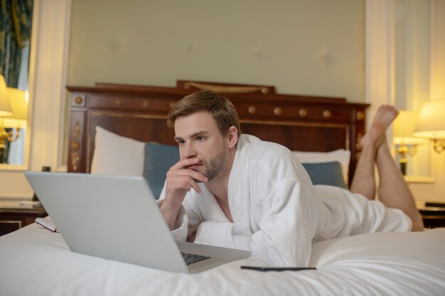 A thoughtful man using a computer while staying in the bed