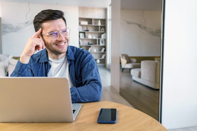 A thoughtful man with a pleasant smile works at a laptop in a tastefully decorated