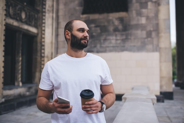 通りでコーヒーを飲むスマートフォンを持つ思いやりのある男