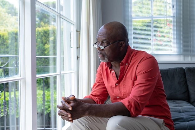 thoughtful mature african american man looking though window while sitting at home, copy space