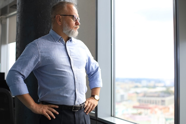 Thoughtful mature business man in a corporate suit looking away while standing near the window.