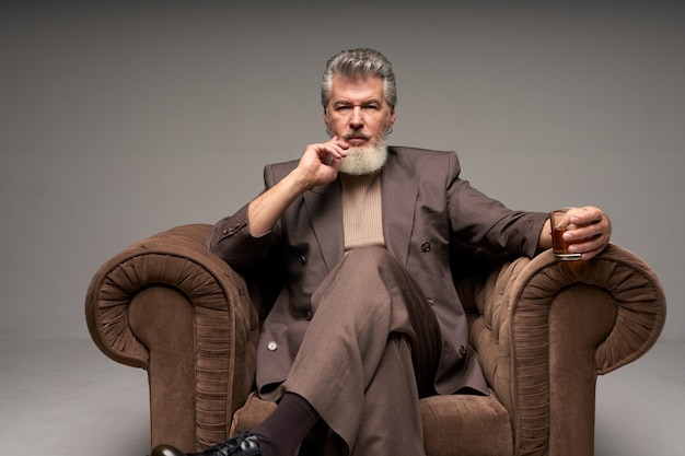 Thoughtful mature businessman with beard wearing elegant suit looking at camera holding a glass of