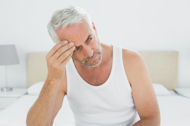 Thoughtful mature man sitting in bed