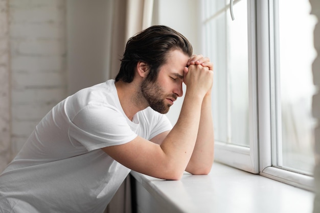 Thoughtful millennial guy standing next to window at home