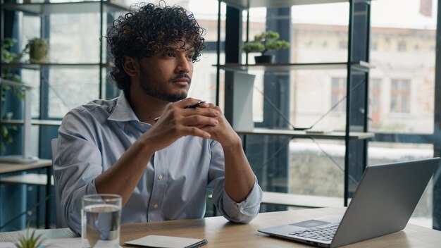 Thoughtful pensive arabian businessman working with laptop at office desk doubtful indian hispanic