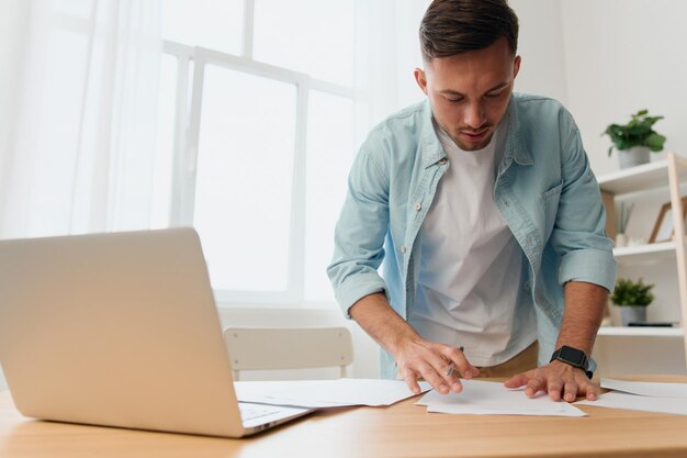 Thoughtful pensive handsome stylish young businessman deals\
with documents and papers for work project on office table copy\
space for ad remote job technology and career profession\
concept