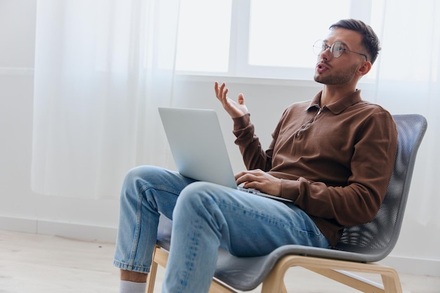 Thoughtful pensive serious young man in eyewear raise hand up\
thinking about best solution for project sitting in chair at home\
remote job distant work communication modern profession\
concept