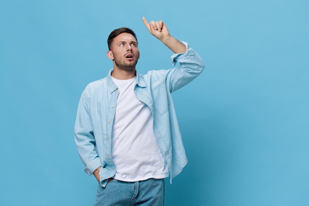 Thoughtful pensive tanned handsome man in casual basic tshirt\
point finger up have good idea posing isolated on blue studio\
background copy space banner mockup people emotions lifestyle\
concept