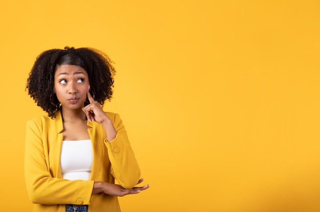 Thoughtful pretty black woman with short hair looking aside at free space for advertisement yellow