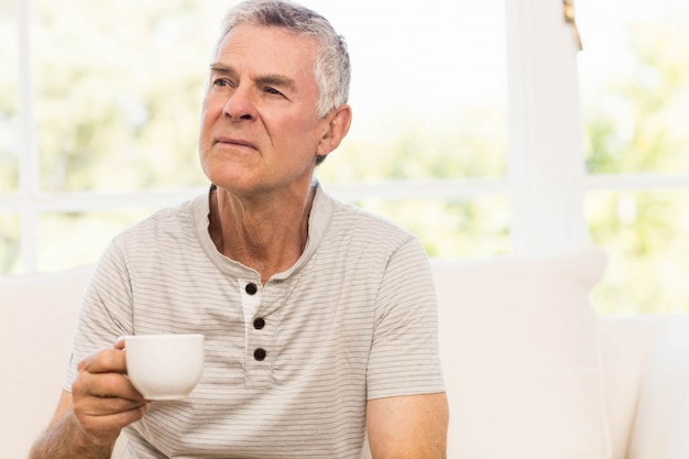 Thoughtful senior man holding mug on the sofa