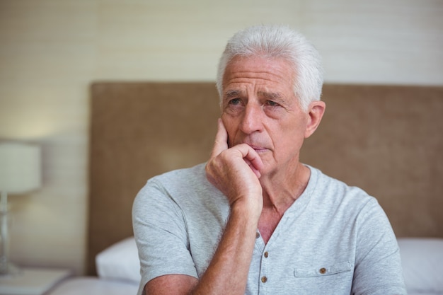 Thoughtful senior man sitting on bed