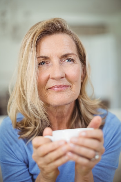 Thoughtful senior woman having cup of coffee in living room