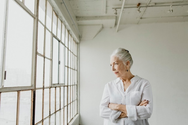 Задумчивая пожилая женщина смотрит в окно в белой комнате