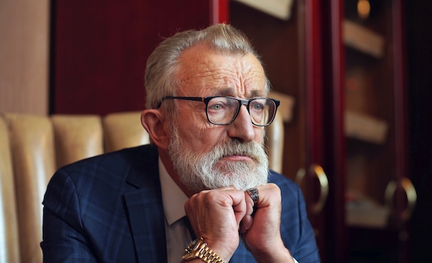 Thoughtful, serious look of the entrepreneur, the owner of the company, elegantly dressed in a stylish suit, photo inside the room, office