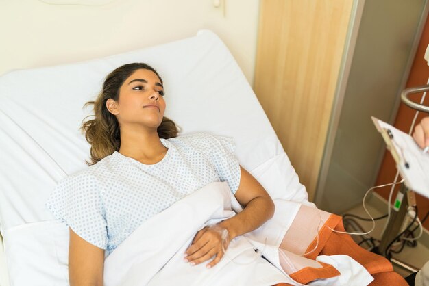 Thoughtful sick patient with IV drip looking away while lying on hospital bed during treatment