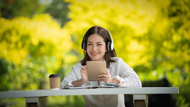 Thoughtful smile Happy woman videocalling online or meeting online working with a tablet in a park