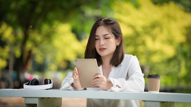 Задумчивая улыбающаяся женщина в парке с помощью умного цифрового планшета Портрет молодого очаровательного бизнеса