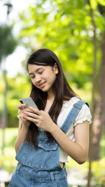 Задумчивая улыбающаяся женщина в парке с помощью смартфона Портрет молодой очаровательной деловой женщины, проверяющей онлайн Деловая работа на своем смартфоне на открытом воздухе в парке на мягком зеленом фоне