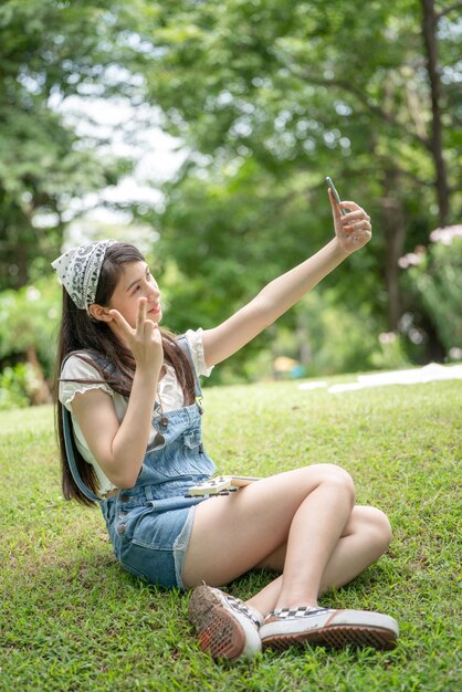 Thoughtful smile woman in park using smart phone for selfie photo Portrait of a young charming