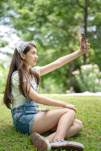 Thoughtful smile woman in park using smart phone for selfie photo Portrait of a young charming