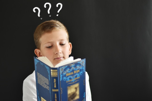 Thoughtful student child at the blackboard with a book