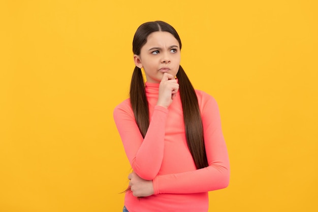 Thoughtful teen girl with long hair on yellow background decision