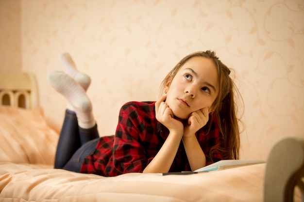 Thoughtful teenage girl lying on bed at bedroom