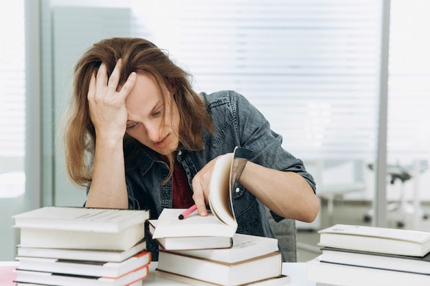 Il ragazzo premuroso e stanco lavora con i libri nella biblioteca