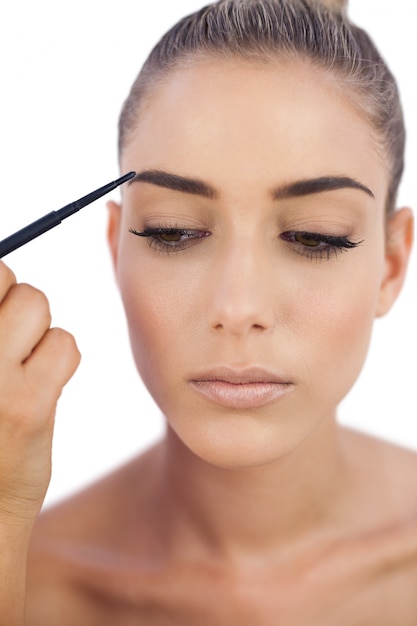 Thoughtful woman applying make up on her eyebrows