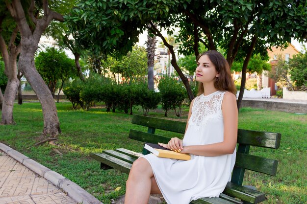 Foto donna riflessiva con un libro in mano mentre è seduta nel parco